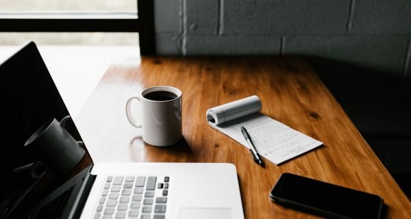 MacBook Pro, white ceramic mug,and black smartphone on table