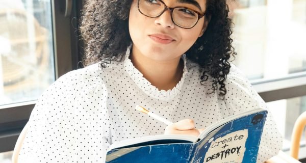 woman in white and black polka dot shirt holding blue and white book