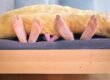 three people underneath yellow bed blanket