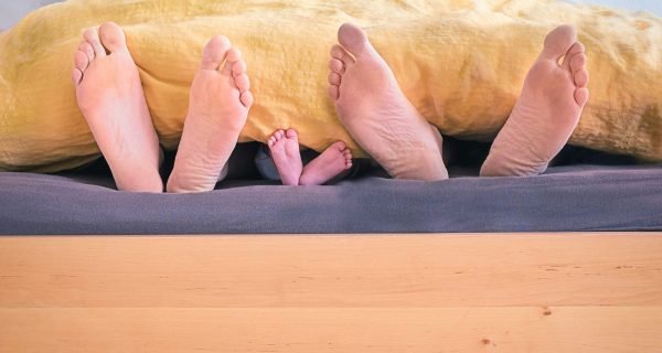 three people underneath yellow bed blanket