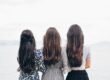 three woman looking back and facing body of water