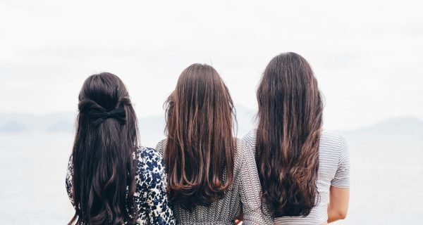 three woman looking back and facing body of water